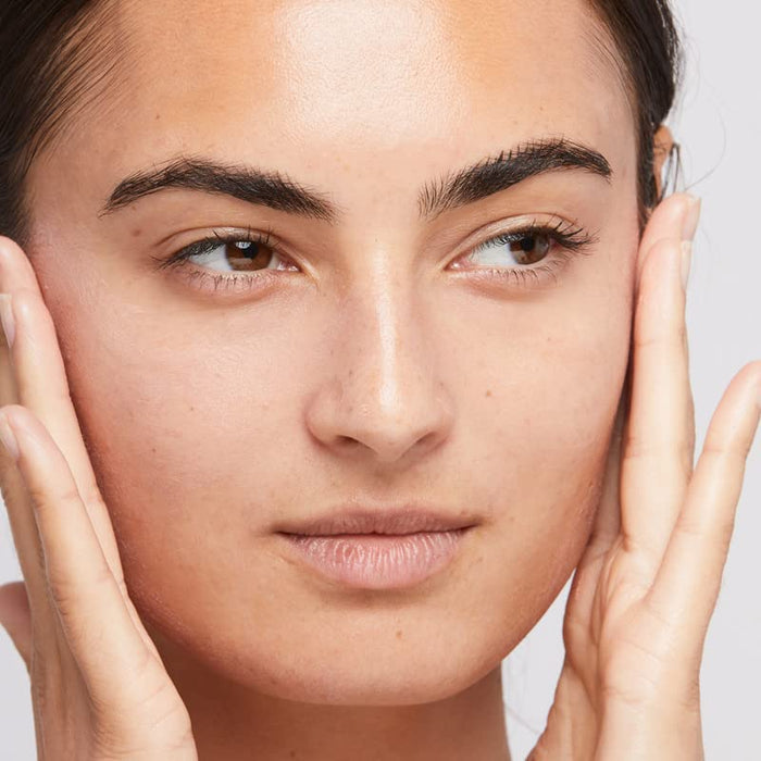 Close-up of a person's face with hands on either side, against a neutral background