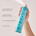 Hand holding a blue can of ENJOY hair spray with product details on a light gray background