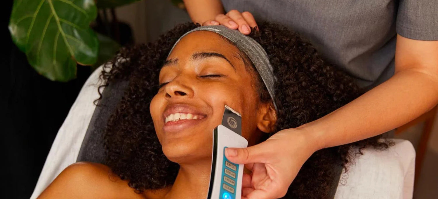 Image of a female laying on a skin table, face up and an esthetician utilizing a ultrasonic skin spatula